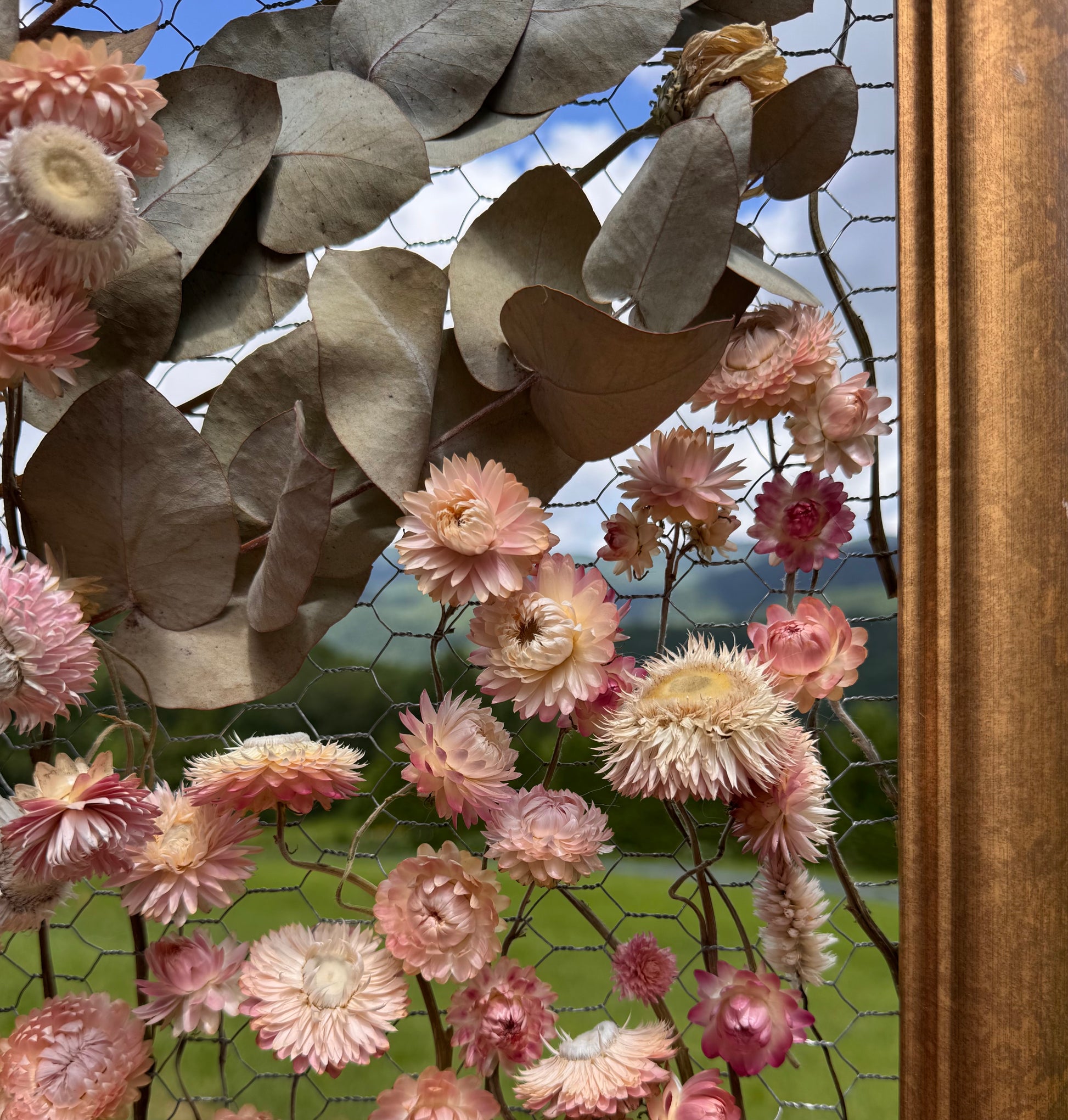 Decorative floral arrangement with pink flowers and green leaves in front of a scenic window.
